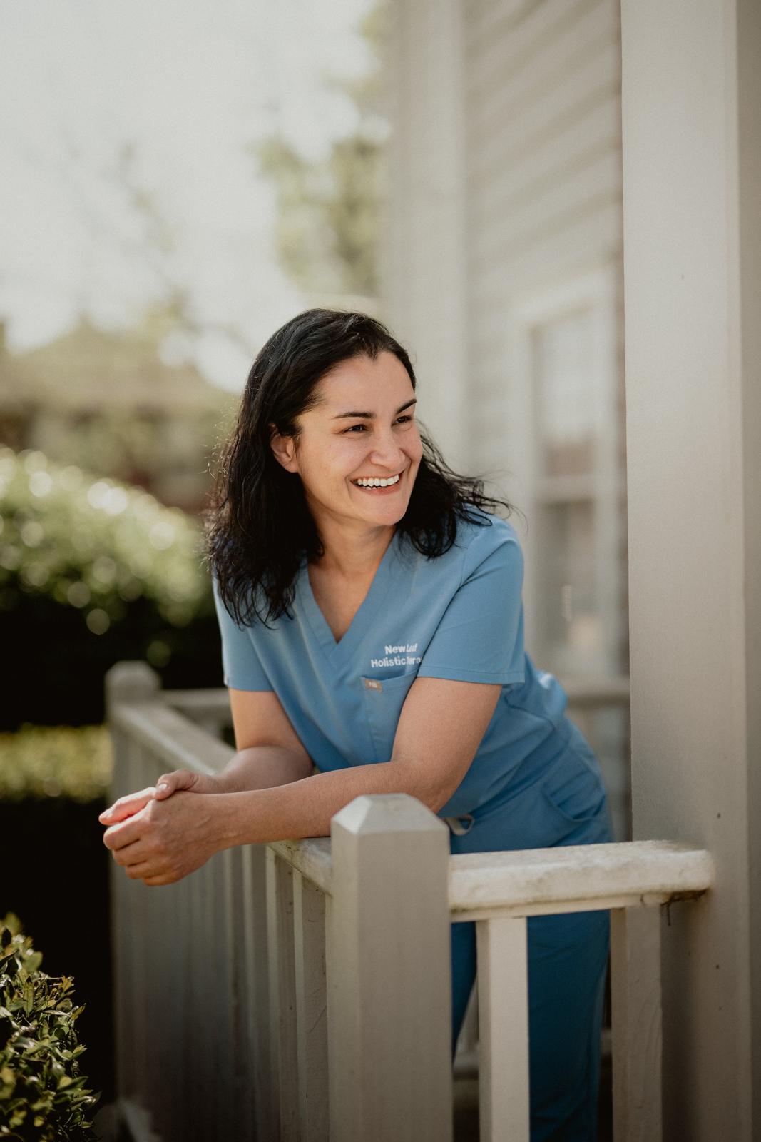 One of our therapists in blue scrubs smiling on the porch railing